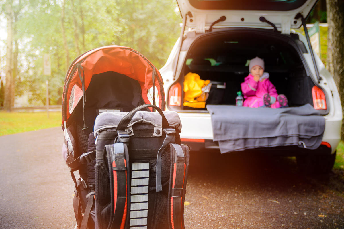 Kraxe vor einem Auto. Baby im Hintergrund