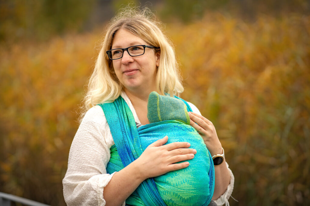 Trageberaterin mit Baby im Tragetuch. Das Baby hat einen physiologischen, gerundeten Rücken. 