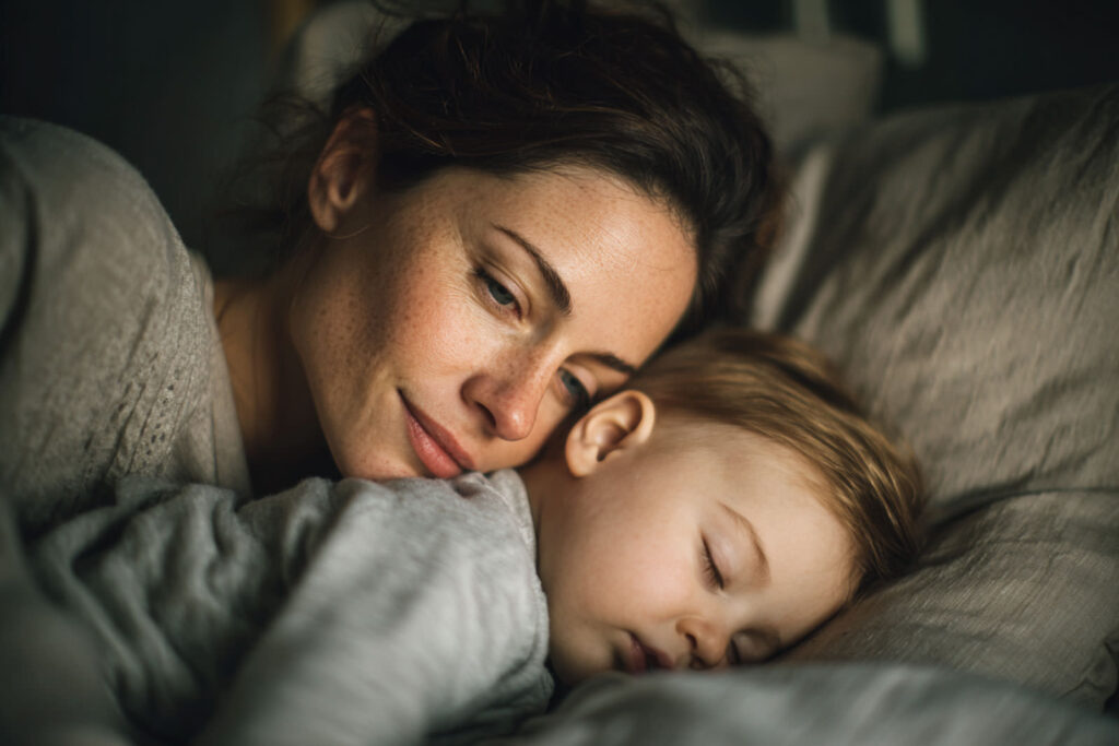 Mutter kuschelt mit Baby im Bett. Baby schläft nur auf dem Arm